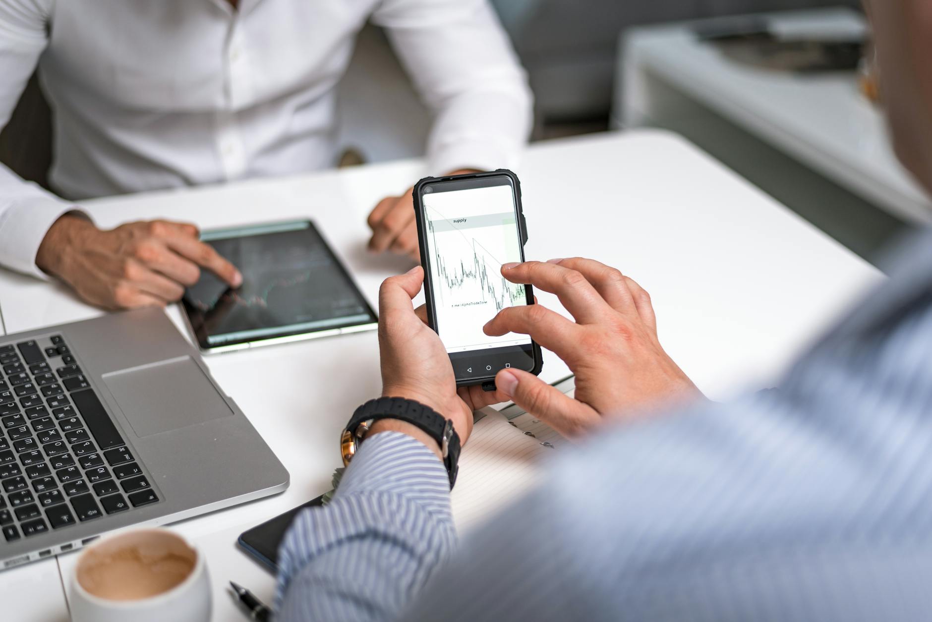 Person using smartphone to check stock trading app with financial charts displayed on screen