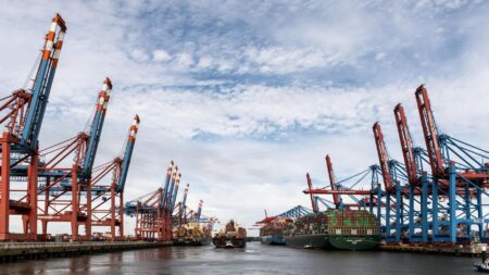 Large cargo ship loaded with shipping containers docked at a busy commercial port