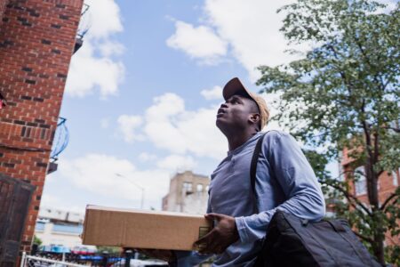 A gig economy delivery worker on a bicycle carrying a food delivery bag in an urban setting