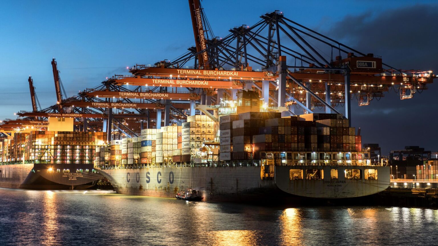 Large cargo ship docked at a busy commercial port with stacked shipping containers