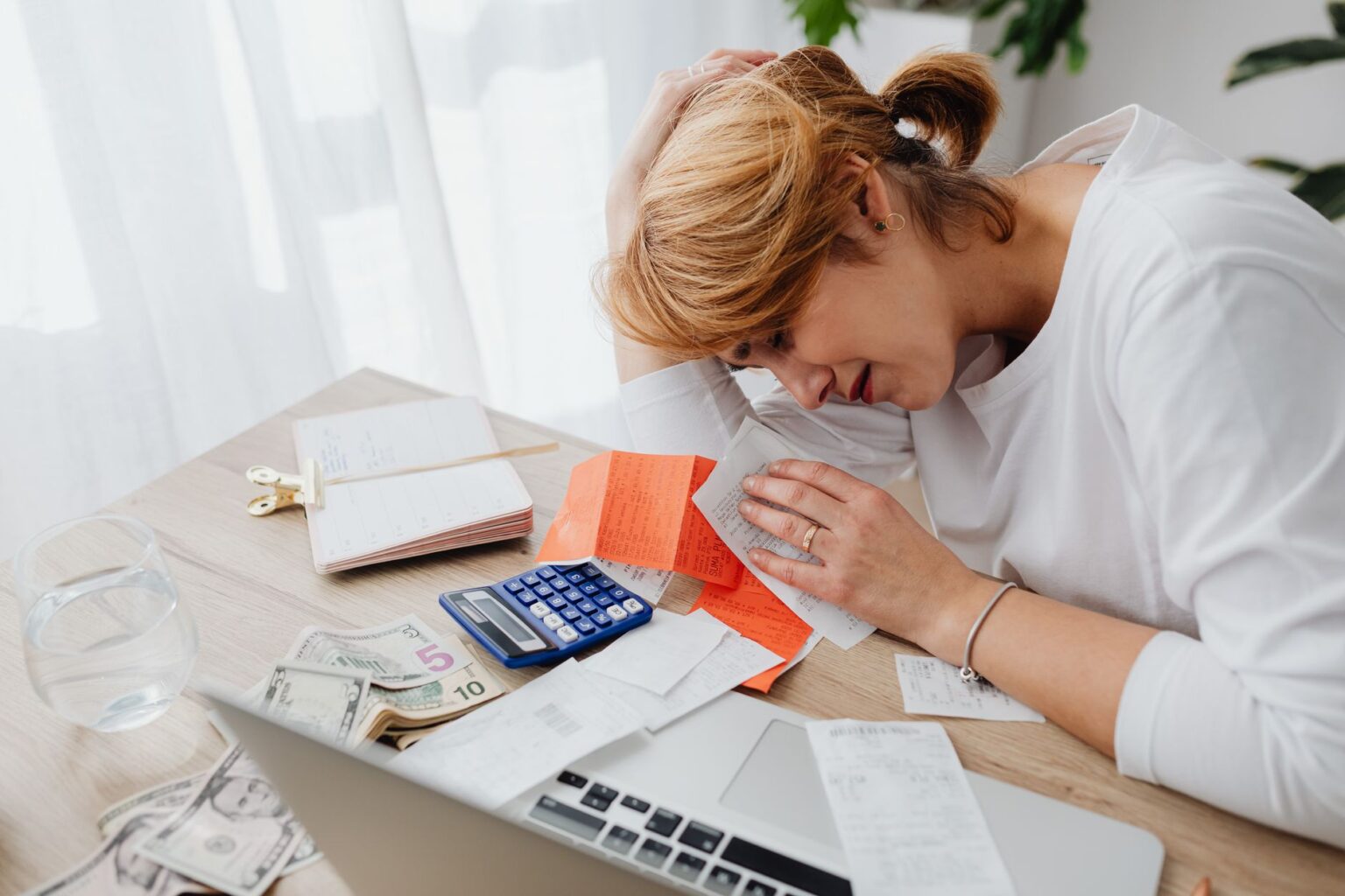 A person sitting at a desk looking stressed while reviewing financial documents and bills