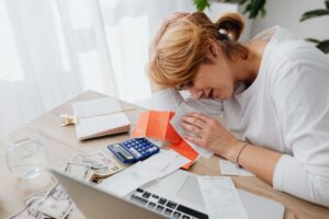 A person sitting at a desk looking stressed while reviewing financial documents and bills