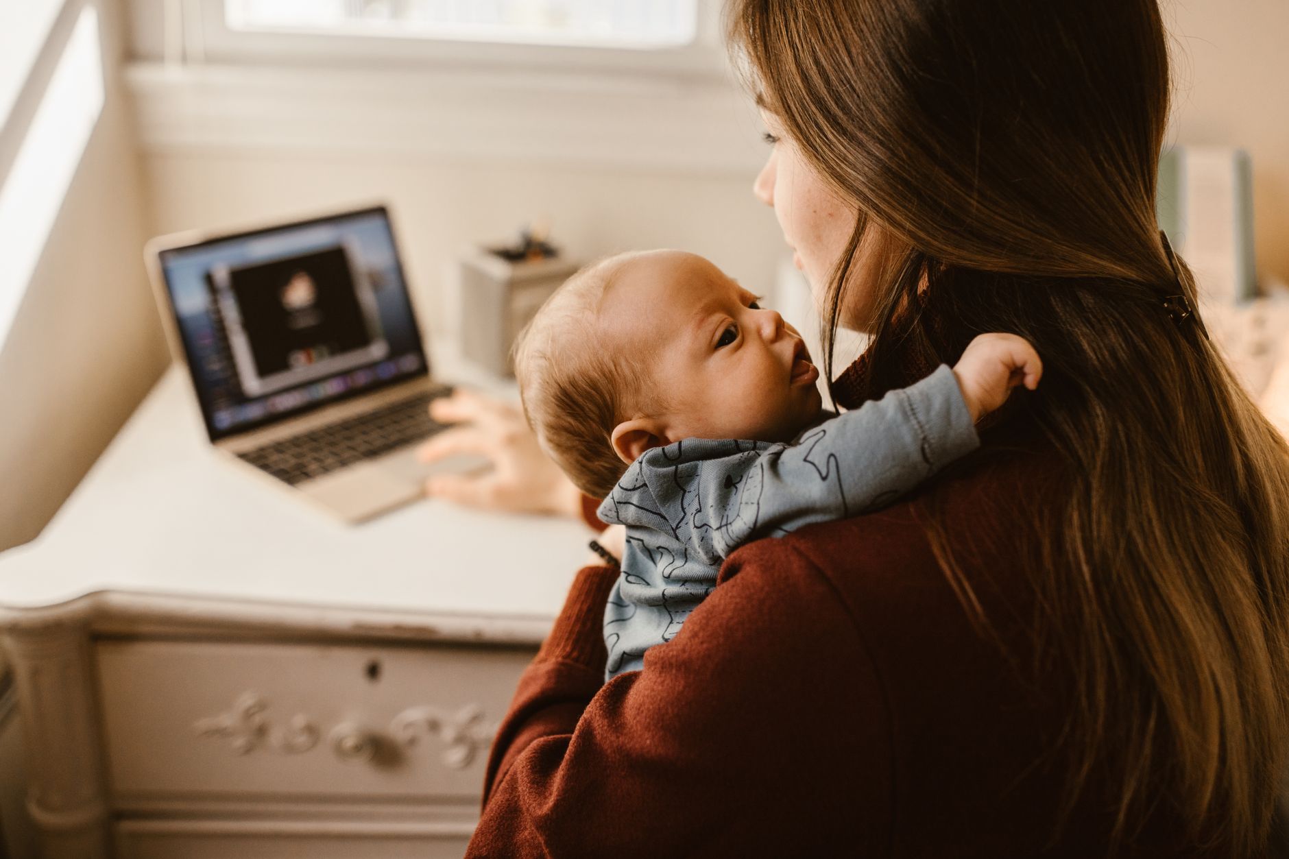Mother working at a desk while managing childcare responsibilities at home